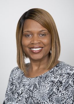 Black woman with shoulder length light brown hair and black and white blouse looks at the camera and smiles