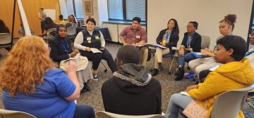 10 students holding a range of identities sit in a circle discussing.