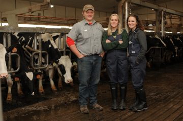 Three animal science students in front of a cow feeding trough